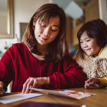young pretty mom writing greeting card for family with her lovely daughter at home