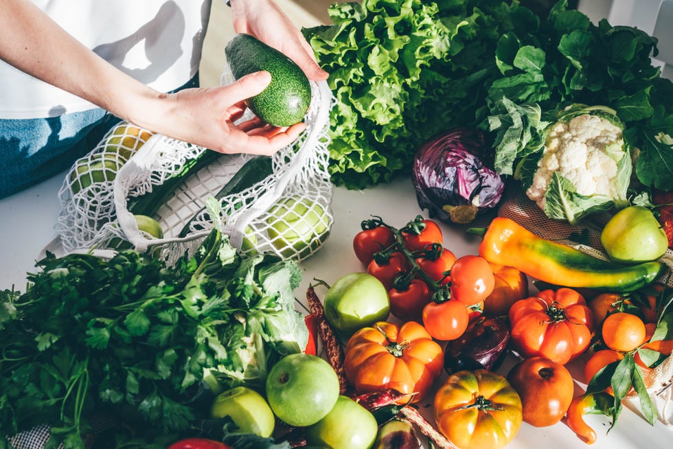 young woman returned with purchases from grocery store takes fresh organic vegetables out of mesh bag putting on kitchen table at home close view