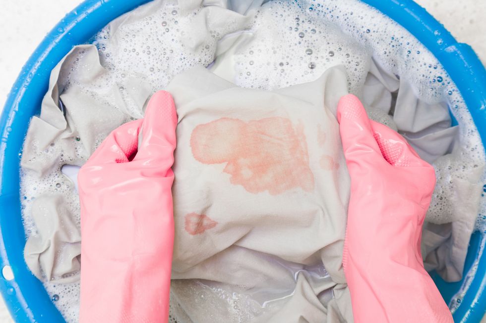 hands in rubber protective gloves washing sheet with blood stain in blue basin point of view shot closeup top down view