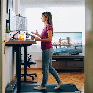 woman working from home at standing desk is walking on under desk treadmill