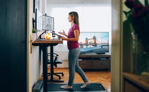 woman working from home at standing desk is walking on under desk treadmill