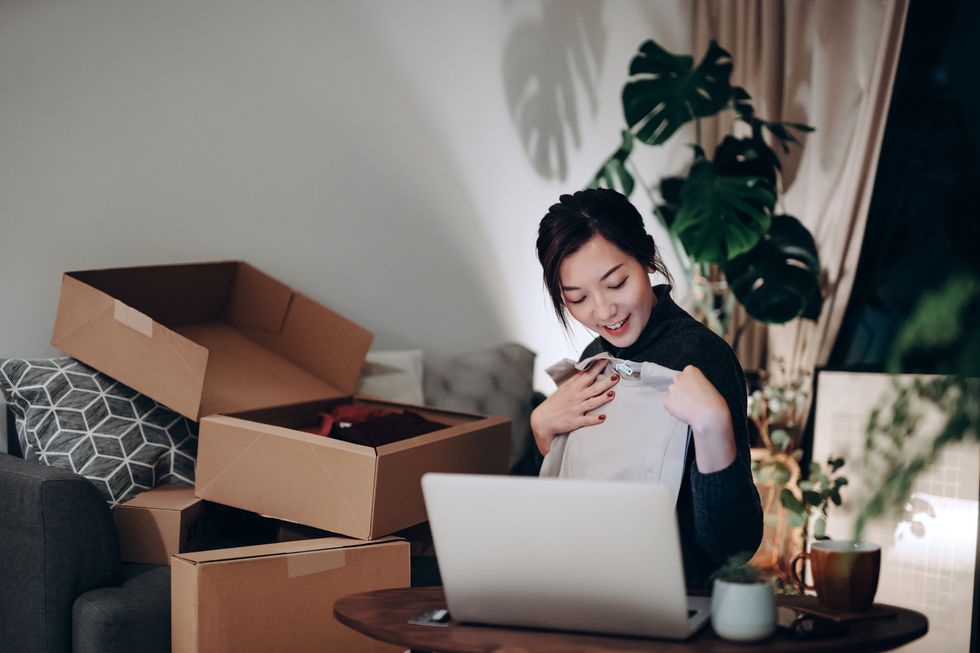 young asian woman unboxing new purchase clothings from cardboard box that received from her online shopping retail delivery at home she is happy and excited to see the content from the box online shopping, trustworthy parcel delivery service
