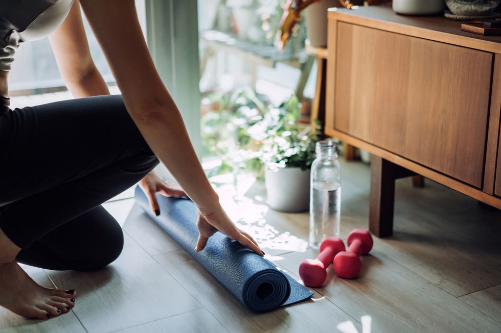 close up of young asian sports woman practicing yoga  exercising at home unrolling yoga mat, getting prepare to work out in the fresh bright morning