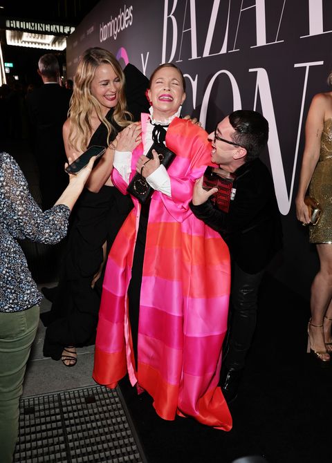 alicia silverstone in black, drew barrymore in a red and pink cape, and christian siriano, also in black, laugh on the red carpet