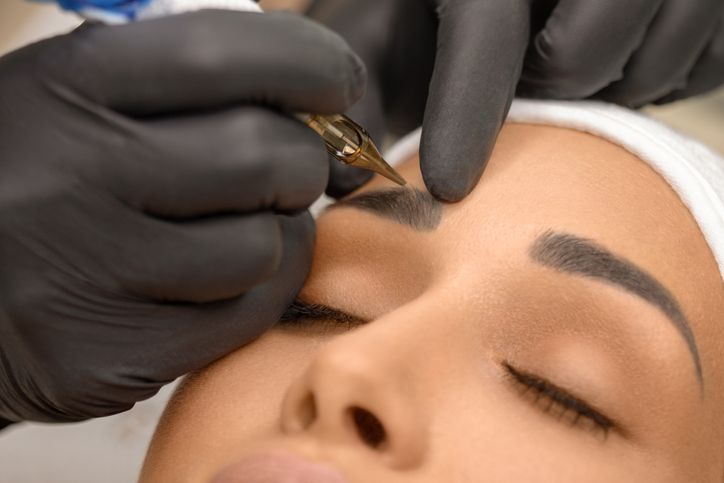make up artist applying permanent make up on eyebrows at beauty treatment beautician contouring and shading young womans eyebrow with special tool