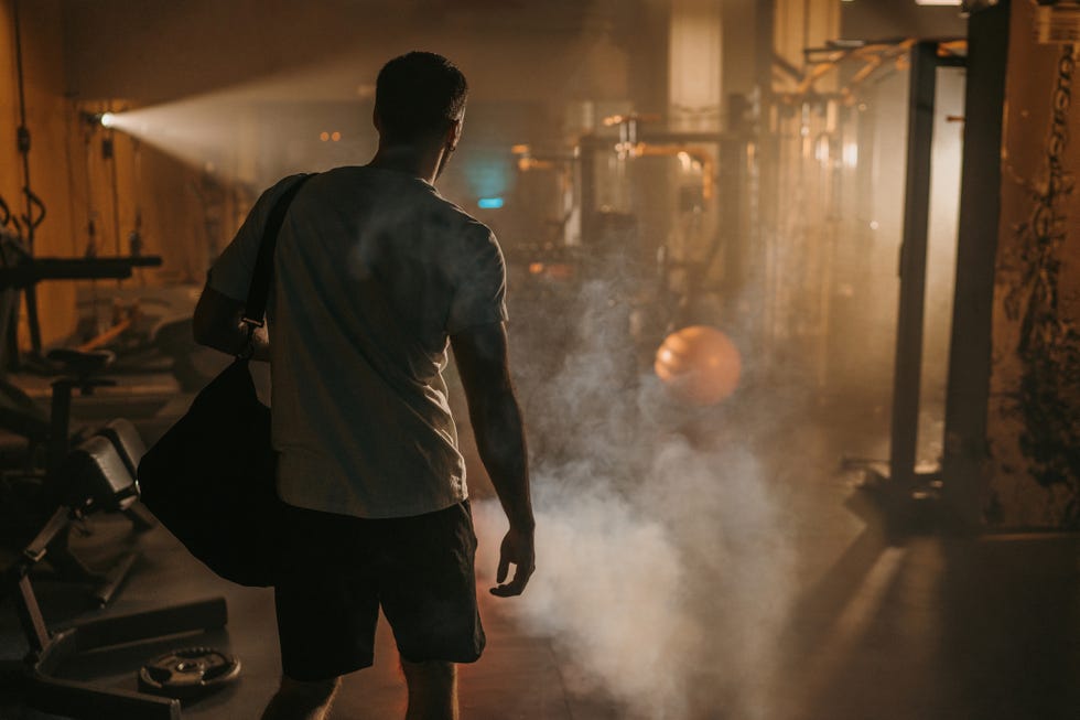 fit man carrying gym bag walking in dark gym filled with smoke alone