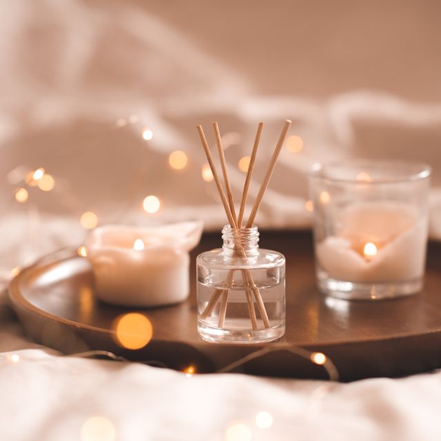 home perfume in glass bottle with wood sticks, scented burn candles on tray in bedroom close up over white aromatherapy cozy atmosphere lifestyle winter warm xmas season good morning
