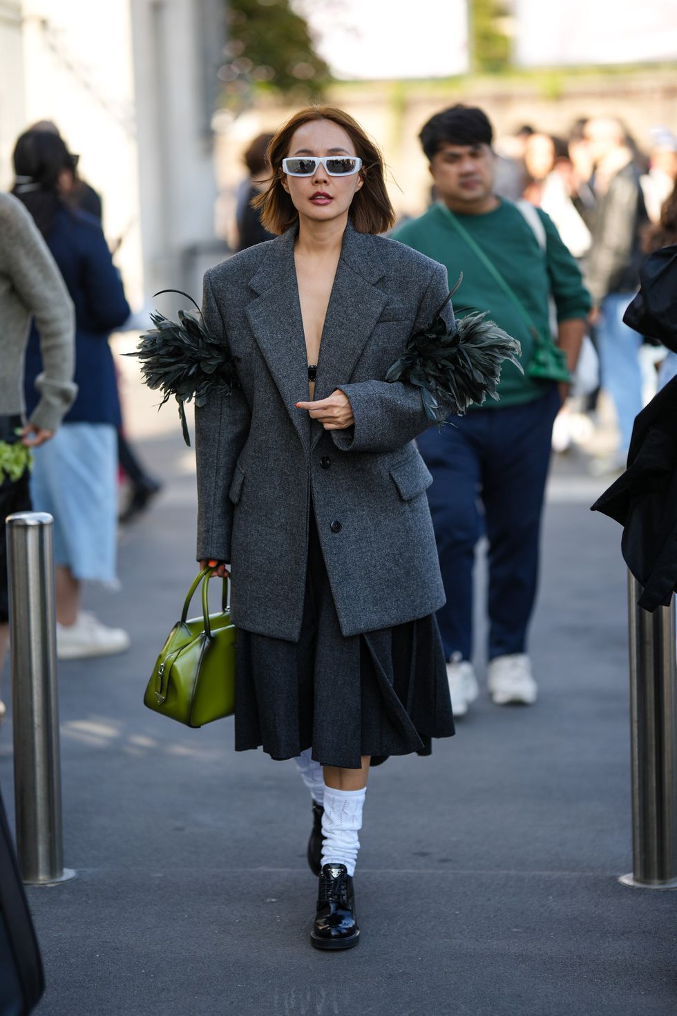 milan, italy   september 22 a guest wears white sunglasses, a black bra underwear, a dark gray oversized blazer jacket with embroidered feathers sleeves, a dark gray knees pleated skirt, a green and black tie and dye print pattern shiny leather handbag from prada, white socks, black shiny leather block heels loafers from prada , outside prada, during the milan fashion week   womenswear springsummer 2023 on september 22, 2022 in milan, italy photo by edward berthelotgetty images