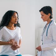 african american female patient touching belly and telling a mature worried doctor about stomachache at hospital appointment healthcare specialist showing concern about symptoms