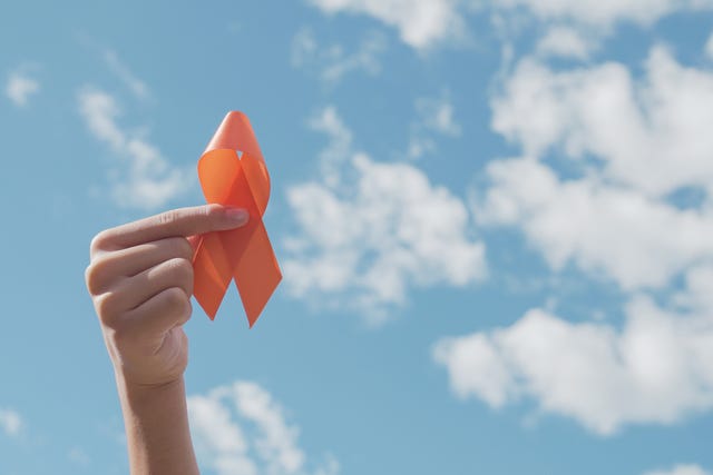hands holding orange ribbon over blue sky,  leukemia cancer and multiple sclerosis, copd and adhd awareness, world kidney day