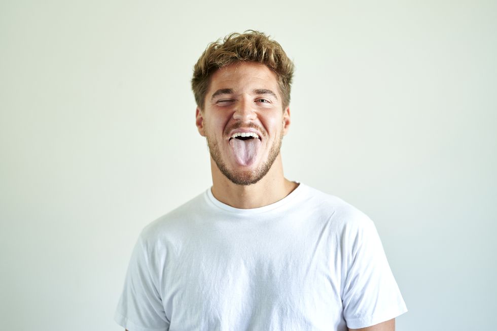 portrait of man sticking out tongue in front of white wall