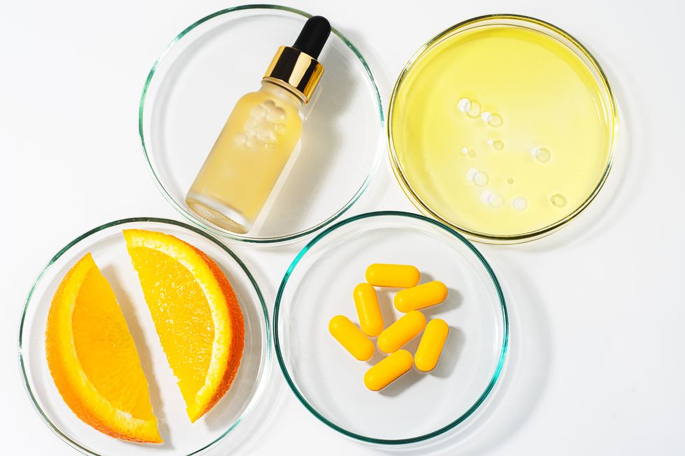 trendy beauty concept of vitamin c serum in cosmetic bottle with dropper and petri dishes with slices of orange fruit, oil and pills with vitamin c on white background organic spa natural skin care product with herbal ingredients flat lay copy space