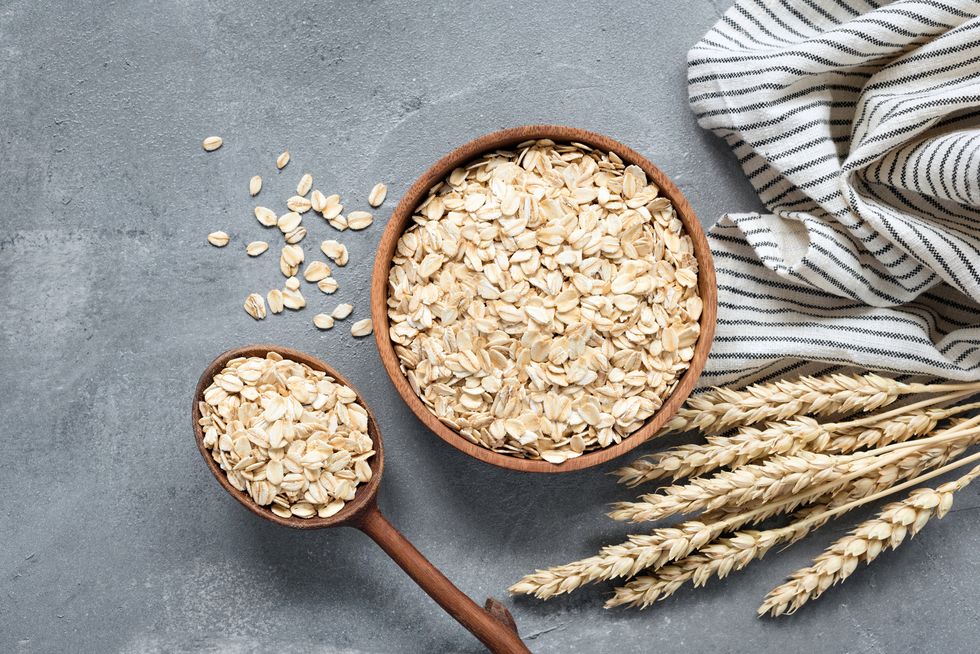 oats, rolled oats or oat flakes in wooden bowl and wooden spoon top view healthy grains, low carb diet food