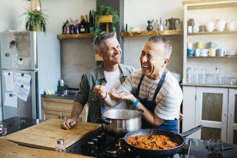 mid adult cheerful gay couple talking and having fun while cooking in a kitchen