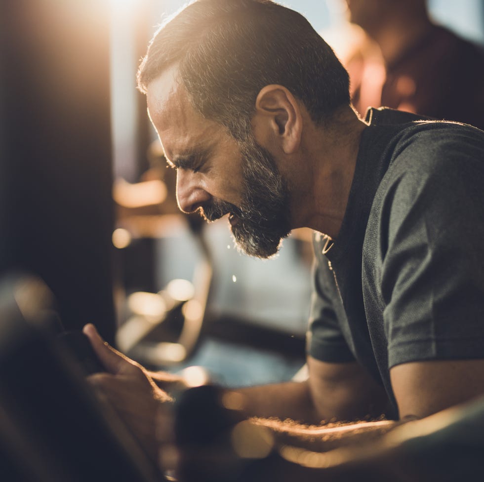 mature man making an effort while riding an exercise bike with his eyes closed in a gym