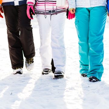 low section of five friends walking along snowy field on winter holiday