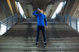 young handsome athlete drinking water on the bridge after running