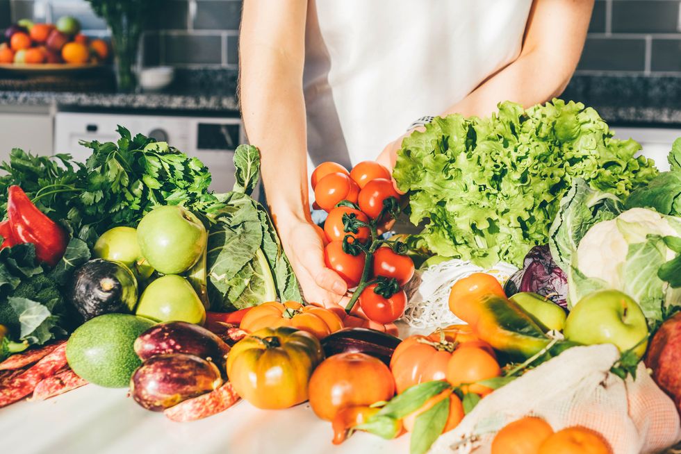 young woman returned with purchases from grocery store takes fresh organic vegetables out of mesh bag putting on kitchen table at home close view