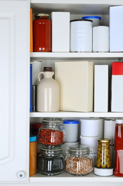 closeup of a well stocked pantry one door of the cabinet is open revealing canned goods, condiments, package foodstuffs, and storage jars