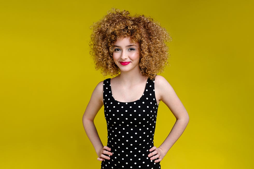 a portrait of a happy teenage girl wearing a polka dot dress standing in front of a yellow background