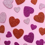 various sizes of glitter heart papers on pink background