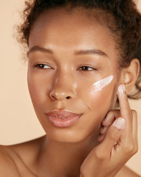 Gesichtshautpflege Frau, die kosmetische Creme auf sauberer, hydratisierter Haut aufträgt Porträt schöne glückliche lächelnde afroamerikanische Mädchenmodell mit natürlichem Make-up, das Gesichtsfeuchtigkeitscreme, Schönheitsprodukt aufträgt
