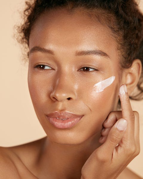 Gesichtspflege. Frau, die kosmetische Creme auf Hautporträt aufträgt Gesichtshautpflege Frau, die kosmetische Creme auf sauberer, hydratisierter Haut aufträgt Porträt schöne glückliche lächelnde afroamerikanische Mädchenmodell mit natürlichem Make-up, das Gesichtsfeuchtigkeitscreme, Schönheitsprodukt aufträgt