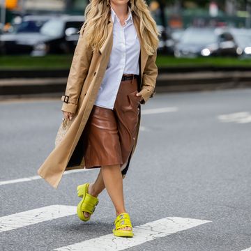 a woman in a long coat and yellow shoes walking across a street
