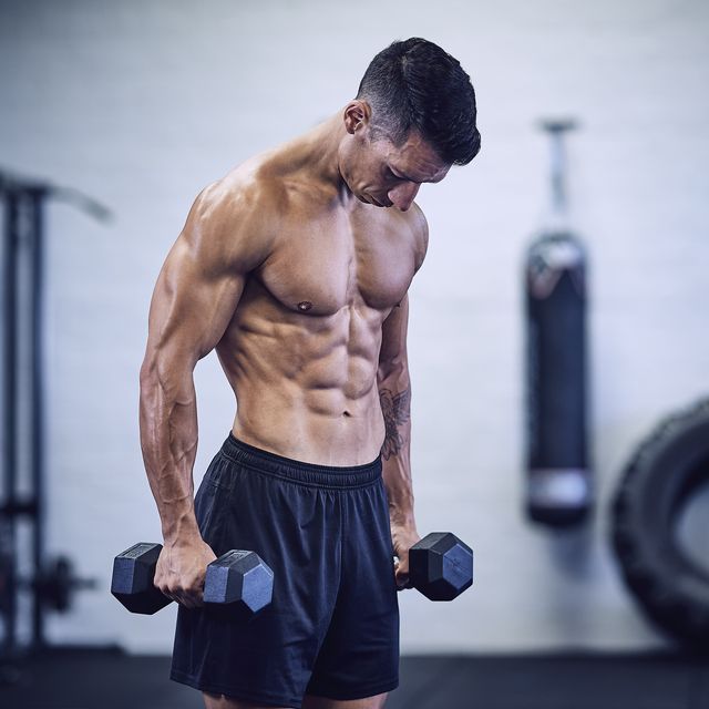 muscular male bodybuilder in industrial gym holding dumbbells