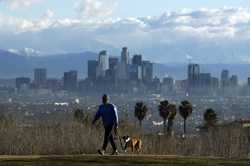 a person walks a dog as snow topped mountains stand behind the los angeles downtown skyline after sunrise following heavy rains as seen from the kenneth hahn state recreation area on december 29, 2020 in los angeles, california photo by patrick t fallon afp photo by patrick t fallonafp via getty images