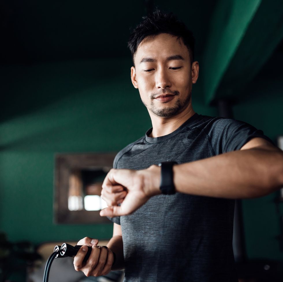 active young asian man exercising at home, using fitness tracker app on smartwatch to monitor training progress and measuring pulse keeping fit and staying healthy health, fitness and technology concept
