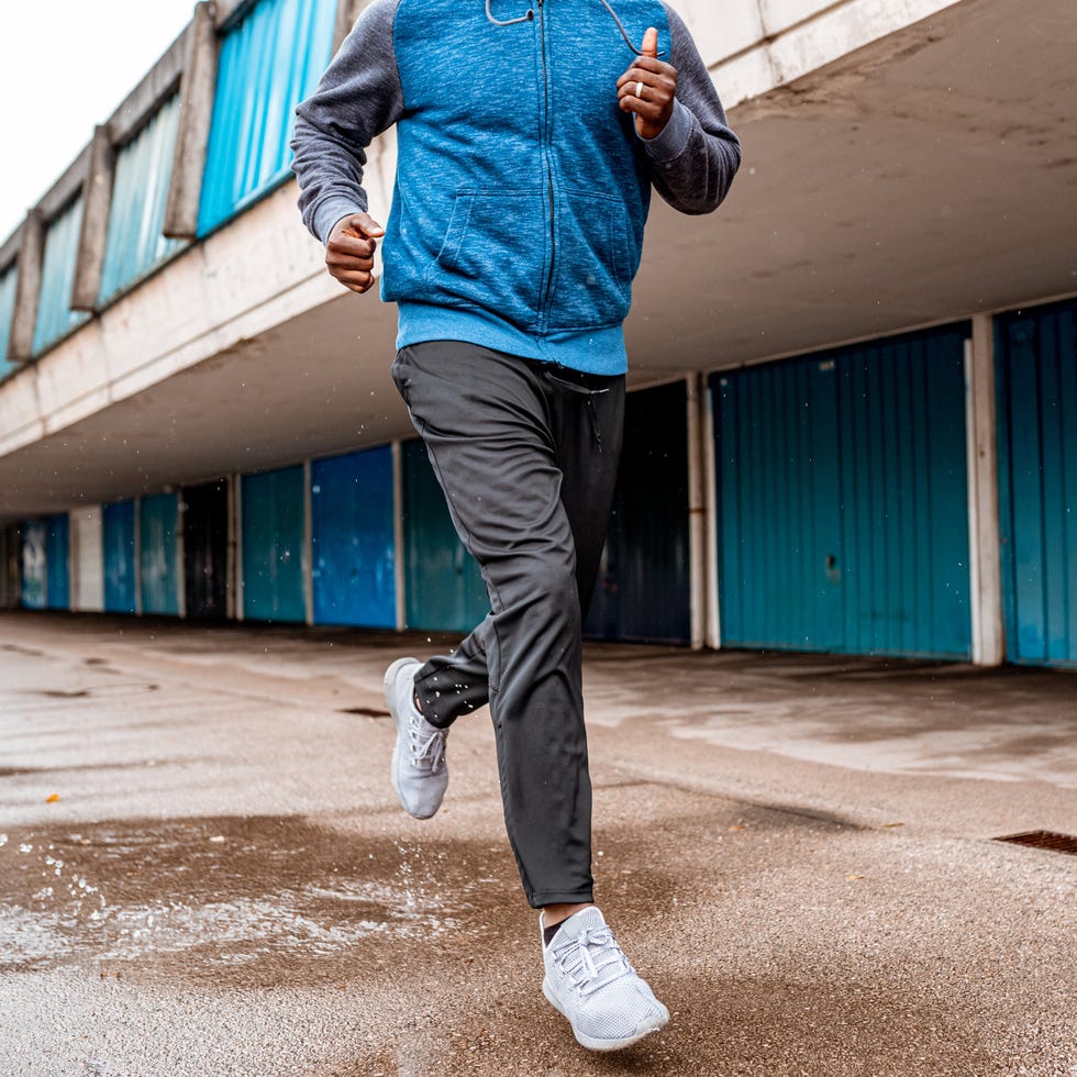 low section of a young african american male athlete running over the puddle next to blue garages