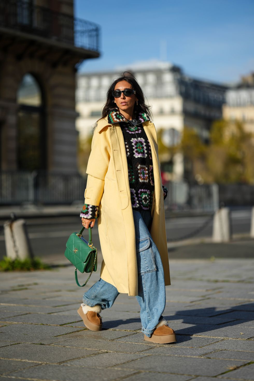 paris, france november 02 gabriella berdugo wears black sunglasses from versace, gold earrings, a black brown green purple white print pattern puffy wool zipper sweater from gestuz, a pale yellow long coat from american vintage, a green shiny leather coco handle handbag from chanel, silver rings, blue denim cargo large pants, camel suede with white sheep interior platform mules from uggs, during a street style fashion photo session, on november 02, 2022 in paris, france photo by edward berthelotgetty images