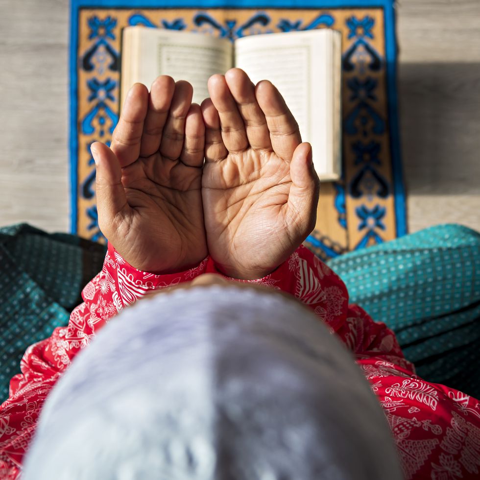 person praying on mat with palms open and quran open in front of them