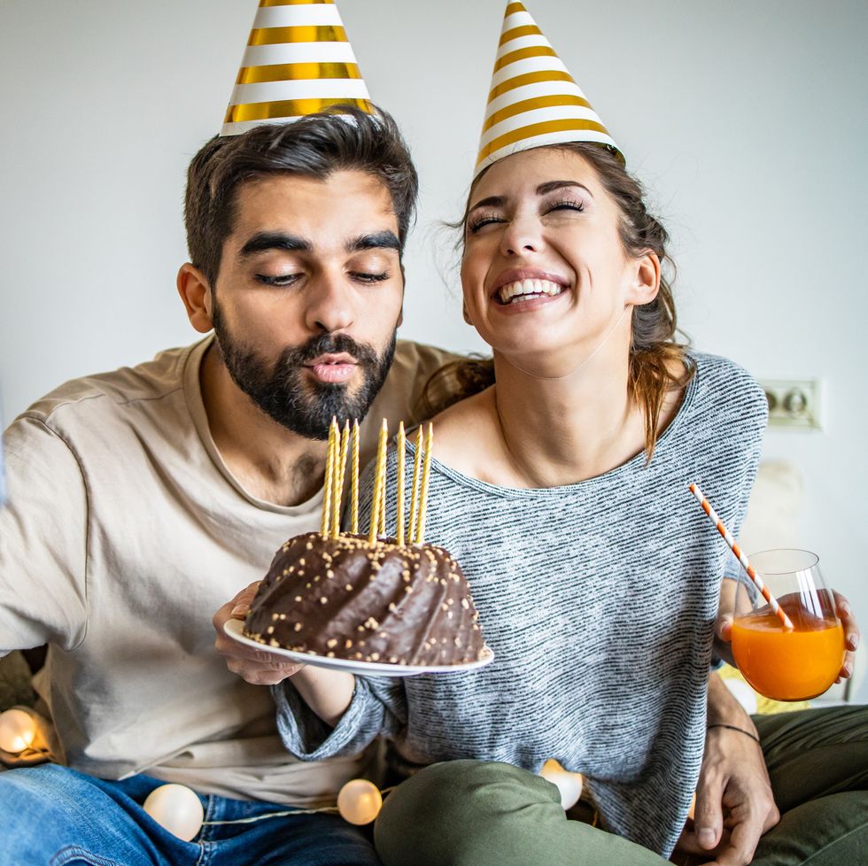 men and woman celebrating birthday at home and young man is blowing birthday candles on the cake