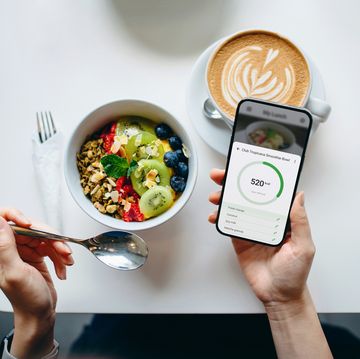 table top view of young woman using fitness plan mobile app on smartphone to tailor make her daily diet meal plan, checking the nutrition facts and calories intake of her breakfast fruit bowl maintaining a balanced diet healthy eating lifestyle