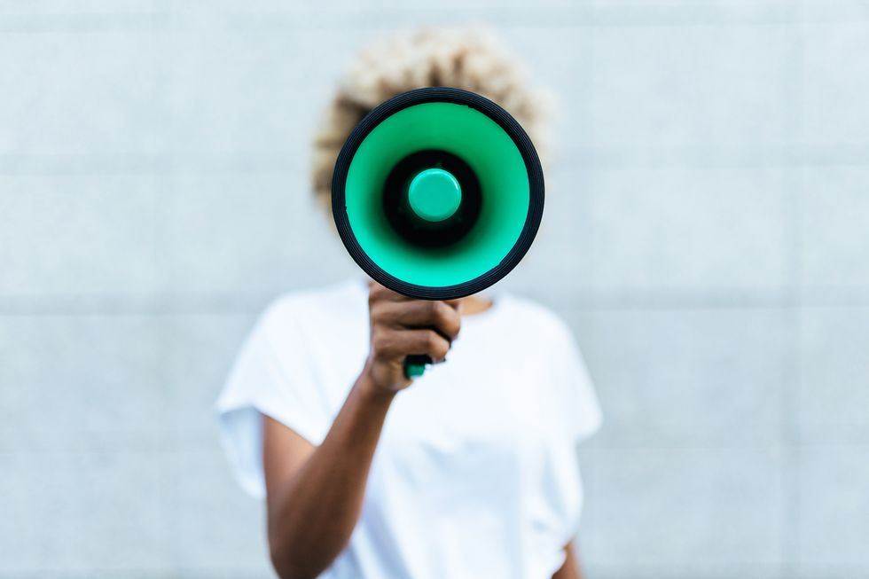 front view of an afro woman shouting through a megaphone to make an announce or protest about something while standing outdoors on the street communication concept