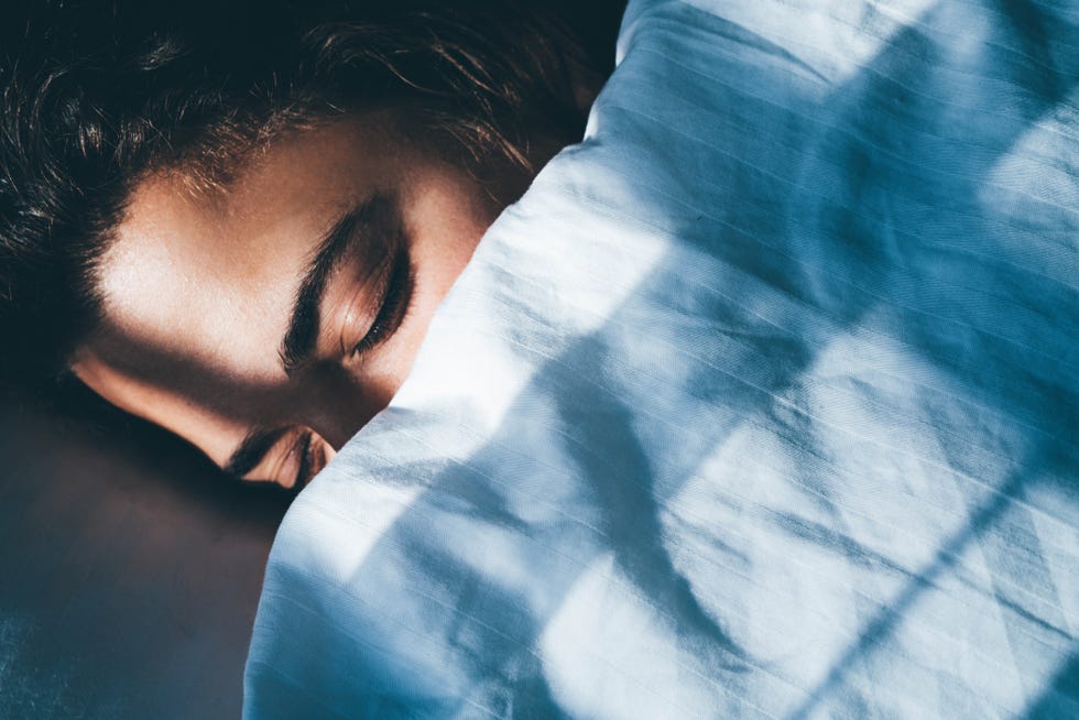 young woman with curly hair sleeps in bed tossing and turning in dream covered with soft blanket in early morning in bedroom at home closeup