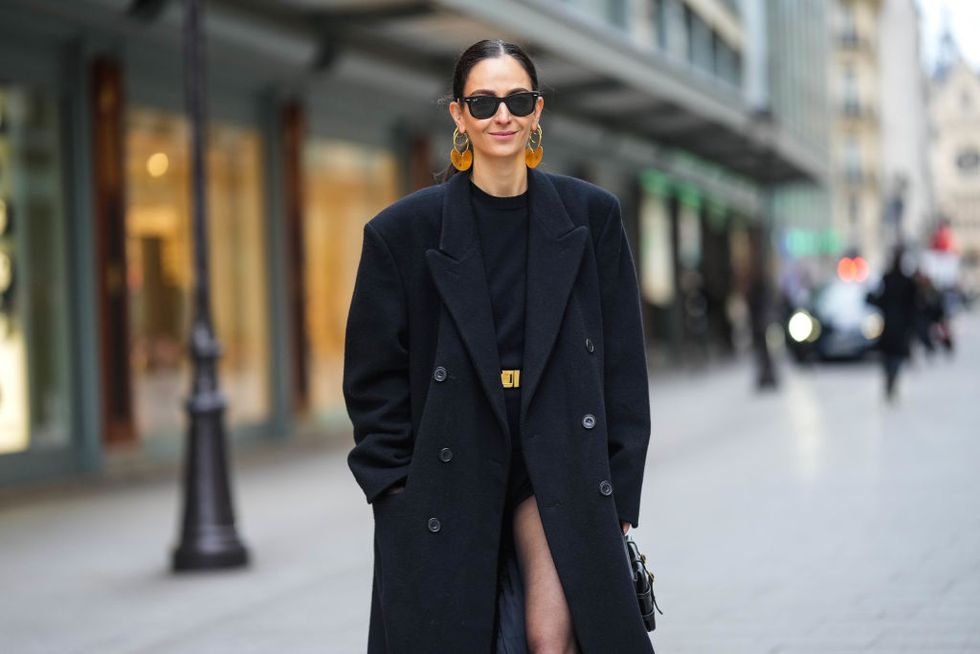 paris, france january 27 ilenia toma wears black sunglasses from ray ban, gold earrings , a black body, a black shiny leather with orange crystal buckle belt, a black wool oversized long coat, a black shiny leather handbag, black tights, outside patou, at la samaritaine, on january 27, 2023 in paris, france photo by edward berthelotgetty images