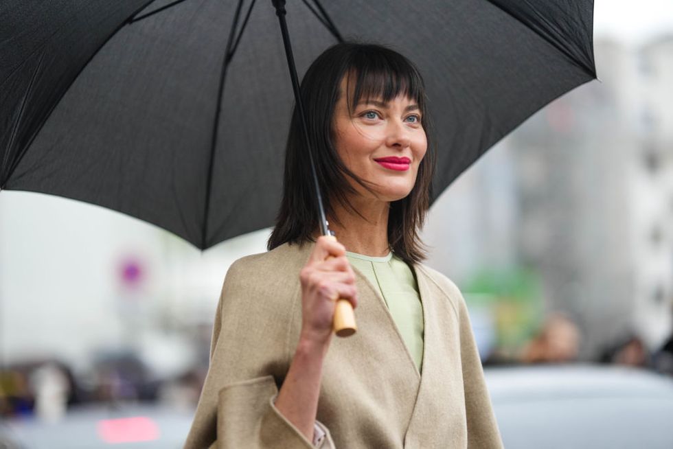 paris, france january 26 a guest wears a black umbrella, a pale green long silk dress, a beige wool with brown silk large belt long coat from fendi, outside fendi, during paris fashion week haute couture spring summer on january 26, 2023 in paris, france photo by edward berthelotgetty images