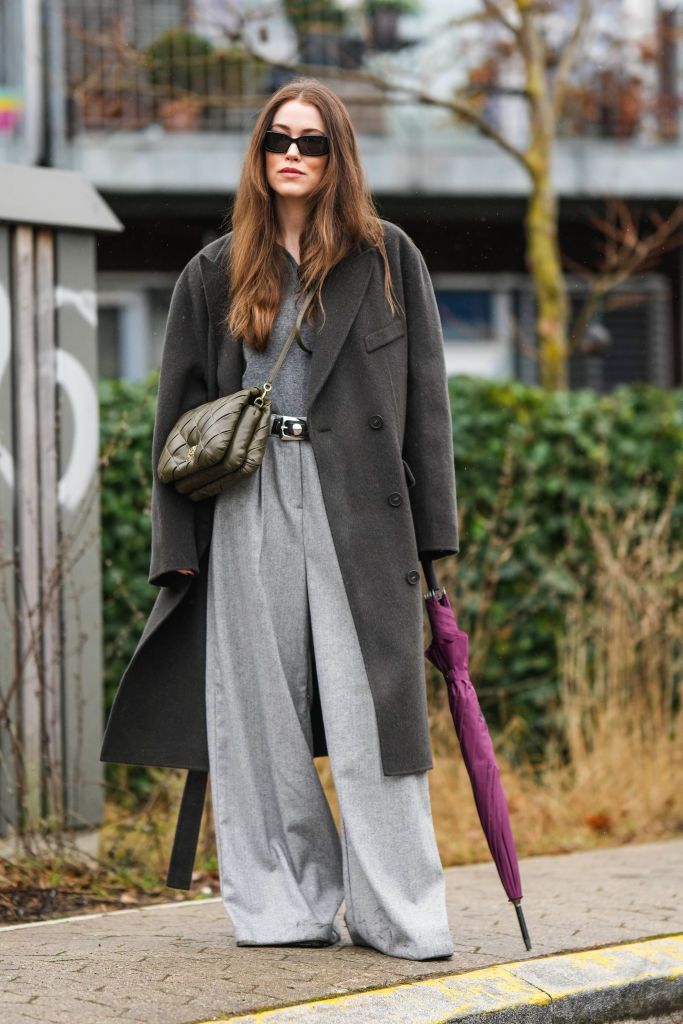 copenhagen, denmark january 31 annabel rosendahl wears black sunglasses, a gray v neck buttoned polo shirt, a dark gray wool long oversized coat, a khaki shiny leather embossed quilted pattern crossbody bag from loewe, pale gray wool large pants, a black shiny leather with silver nailed studded belt, black shiny leather ankle boots , outside aeron , during the copenhagen fashion week autumnwinter 2023 on january 31, 2023 in copenhagen, denmark photo by edward berthelotgetty images