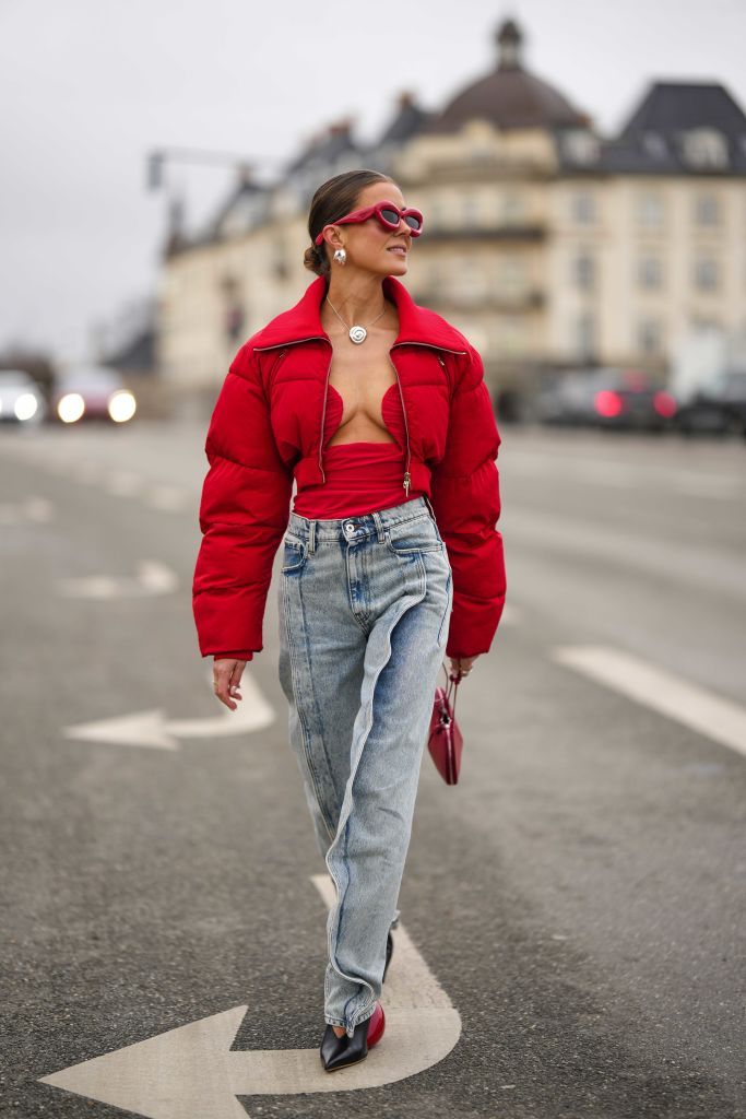 copenhagen, denmark february 01 nina sandbech wears red puffy sunglasses from loewe, silver large earrings, a silver chain and flower pendant necklace, a red heart neck shoulder off body, a red cropped puffer jacket, a red shiny leather zipper handbag in shape of heart, blue faded denim embroidered wavy details large pants, gold rings, black shiny leather pointed balloon heels shoes from loewe, outside operasport , during the copenhagen fashion week autumnwinter 2023 on february 01, 2023 in copenhagen, denmark photo by edward berthelotgetty images
