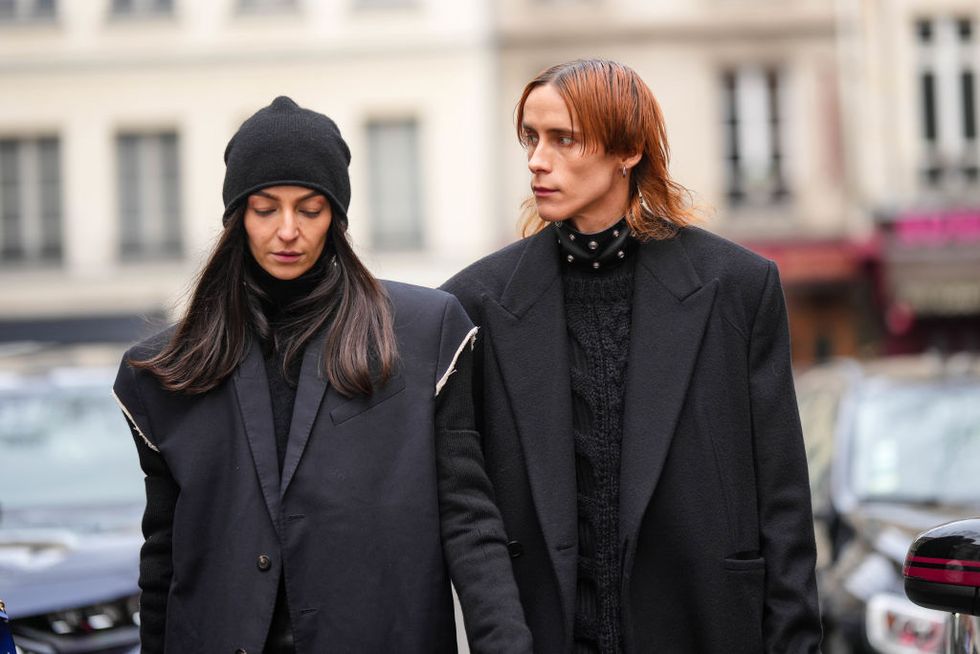 paris, france january 19 a guest l wears a black wool beanie, a black turtleneck pullover, a black shoulder pads long coat, a guest r wears silver earrings, a black shiny leather nailed studded large necklace, a black braided wool pullover, a black long coat, outside rains, during paris fashion week menswear fall winter 2023 2024, on january 19, 2023 in paris, france photo by edward berthelotgetty images