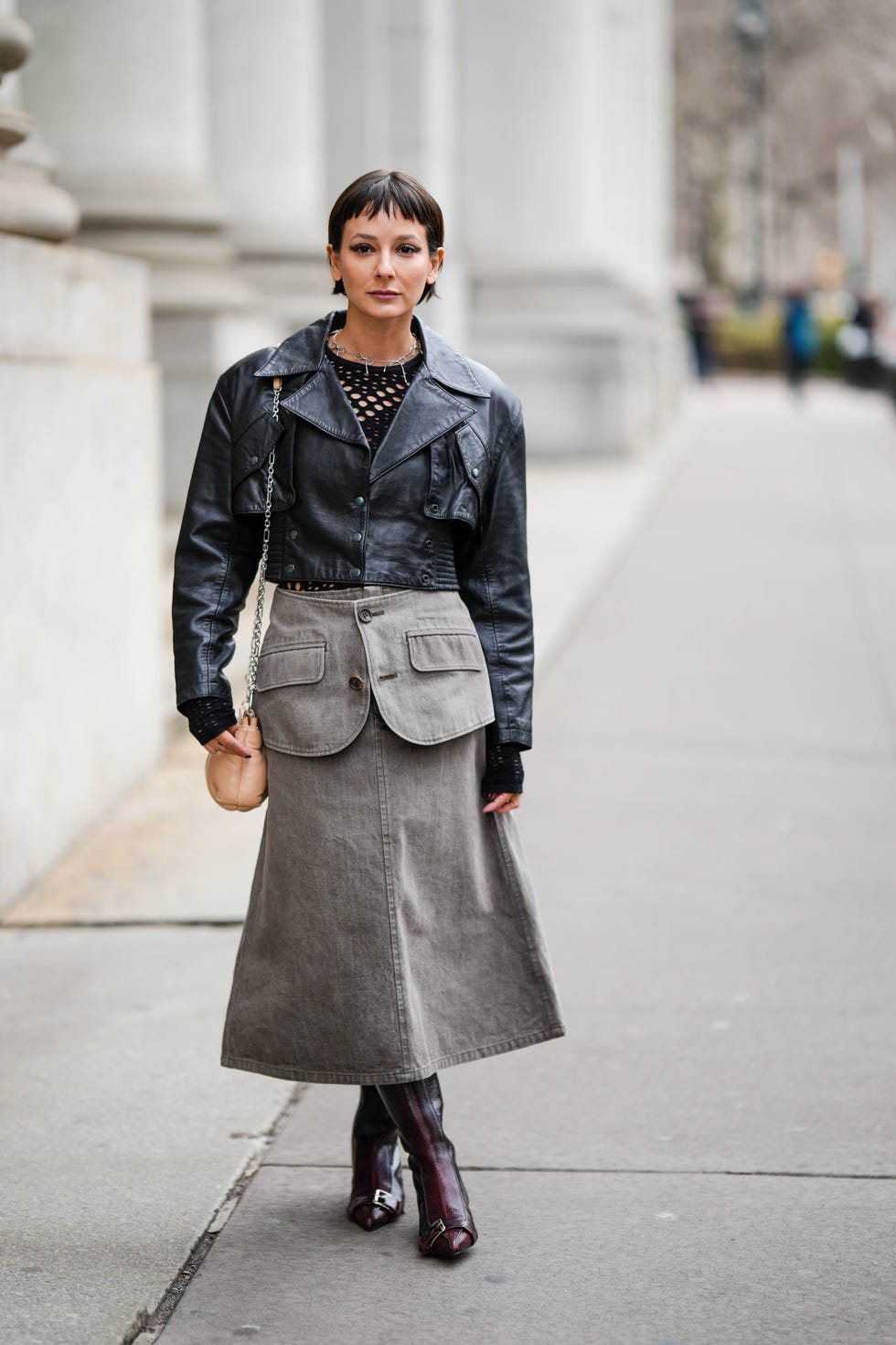 new york, new york february 12 a guest wears a silver knot necklace, a black fishnet mesh body, a black shiny leather buttoned jacket, a beige shiny leather shoulder bag, a pale gray denim midi skirt with a large belt, burgundy shiny leather pointed belted toe cap heels knees boots high boots , outside puppets and puppets, during new york fashion week, on february 12, 2023 in new york city photo by edward berthelotgetty images