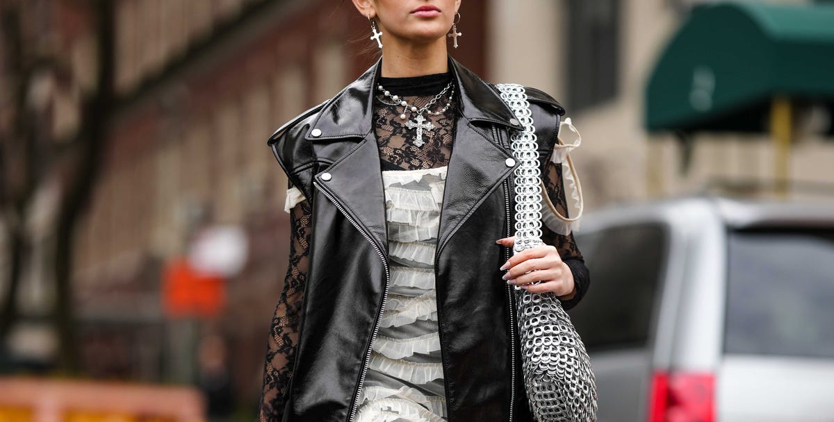 new york, new york february 12 a guest wears silver cross pendant earrings, a silver chain with cross pendant necklace, a black lace print pattern long sleeves legging jumpsuit, a black shiny leather sleeveless oversized zipper gilet jacket, a white tulle ruffled shoulder off long dress, a silver metallic embroidered yoke shoulder bag, black shiny leather platform soles high heels ankle boots , outside jason wu, during new york fashion week, on february 12, 2023 in new york city photo by edward berthelotgetty images