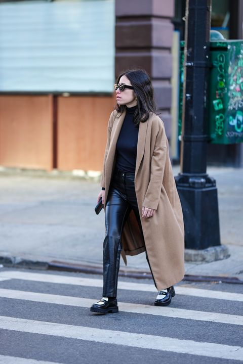 claire stern, new york, new york february 10 a guest wears black sunglasses, gold earrings, a black turtleneck pullover, a beige long coat, black shiny leather pants, black and white shiny leather loafers , outside rodarte, during new york fashion week, on february 10, 2023 in new york city photo by edward berthelotgetty images