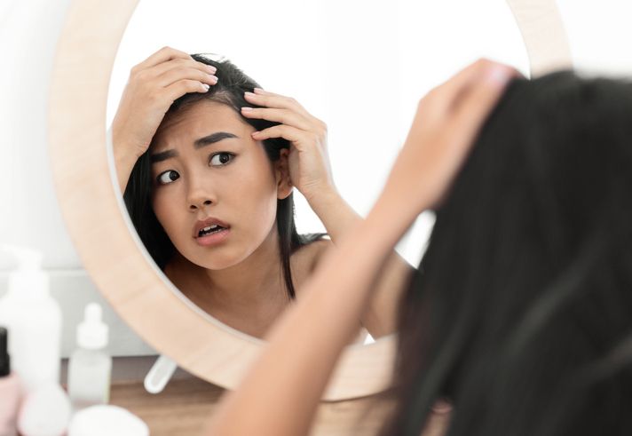 hairloss concept young troubled asian woman checking for thinning hair in mirror at home