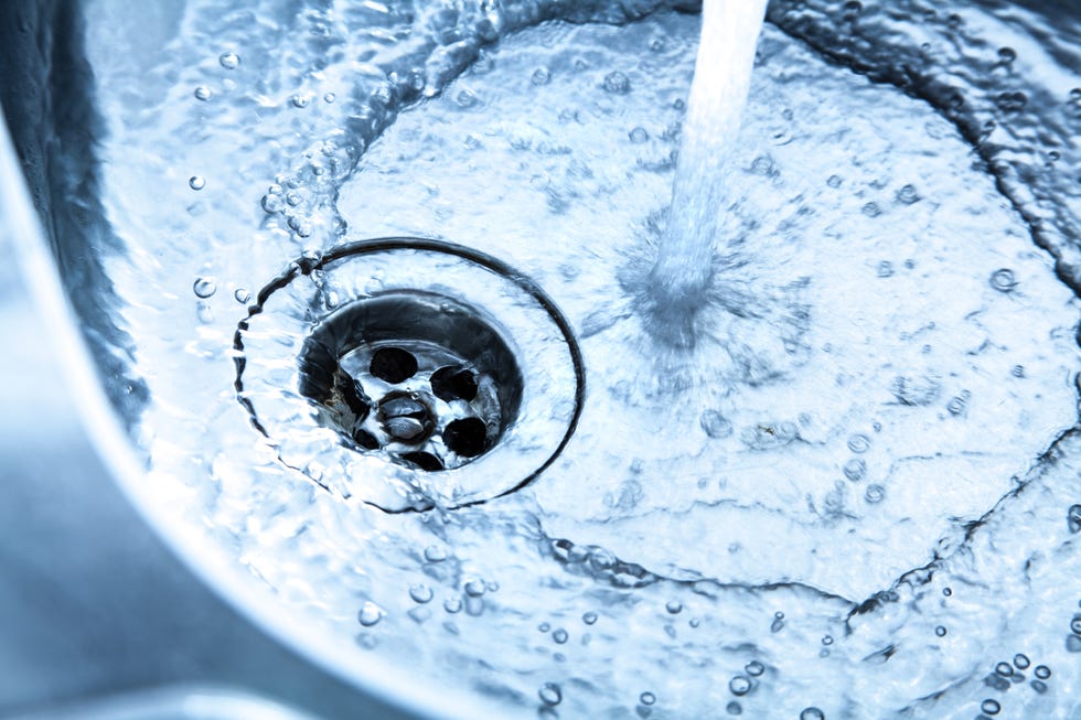 close up of a stainless steel kitchen sink with running water the faucet is turned right up a strong water jet flows into the basin small bubbles and swirls are seen the water flows through the open drain sharp and detailed image blue toned