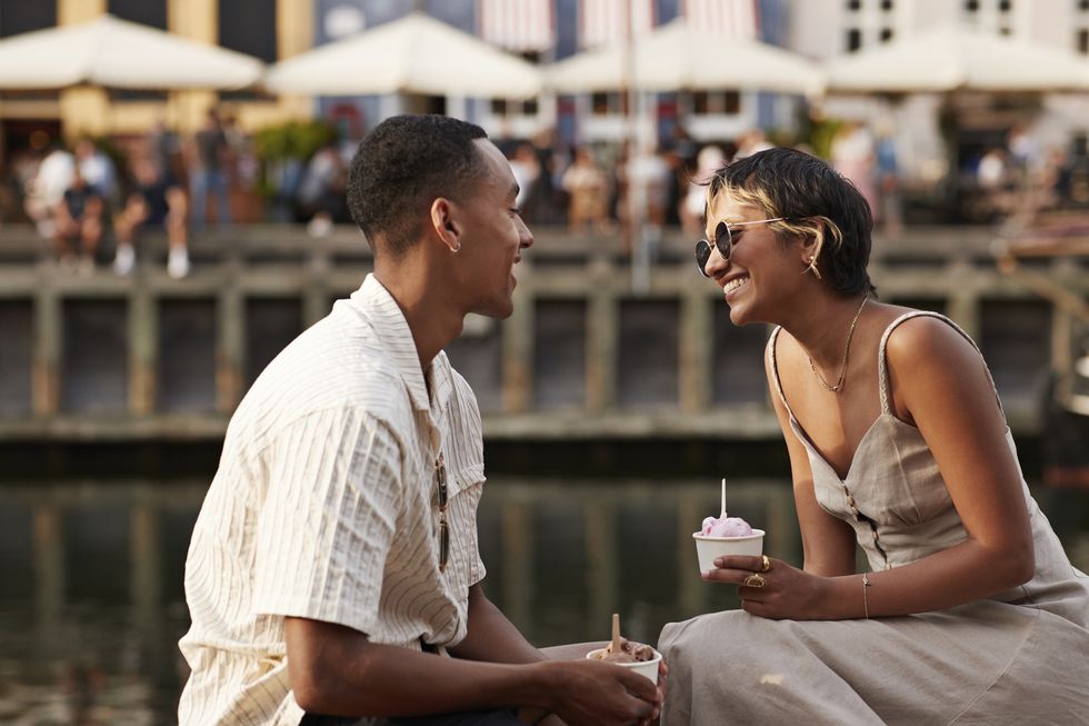 smiling girlfriend and boyfriend with ice cream cups talking to each other on pier
