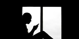 silhouette of 16 year old girl texting backlit at window